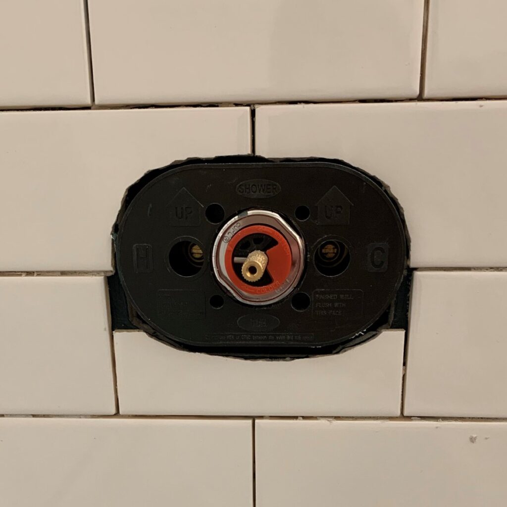 White subway tile cut with nippers around black shower fixture