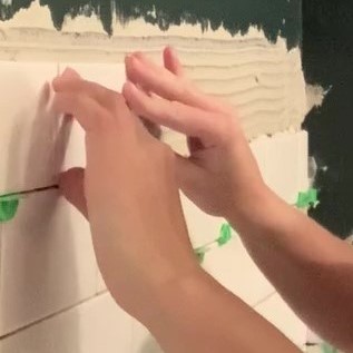 Woman pressing in subway tile to avoid lippage above white bathtub