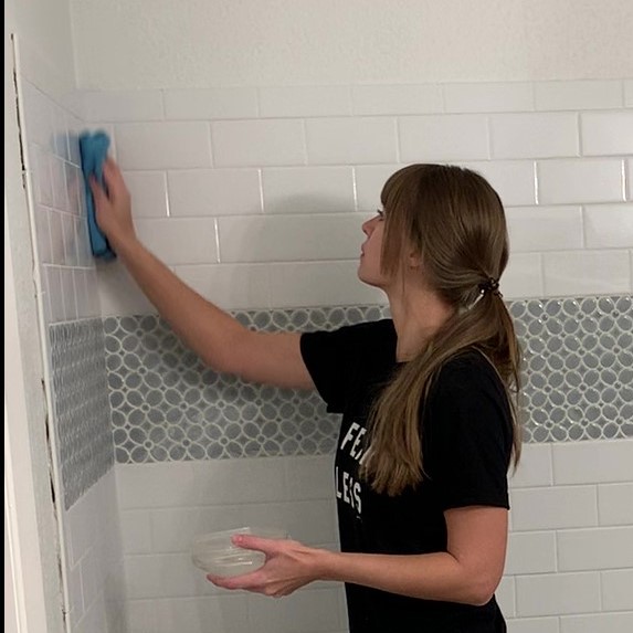 woman wiping grout haze off DIY shower with subway tile and blue flower mosaic tile